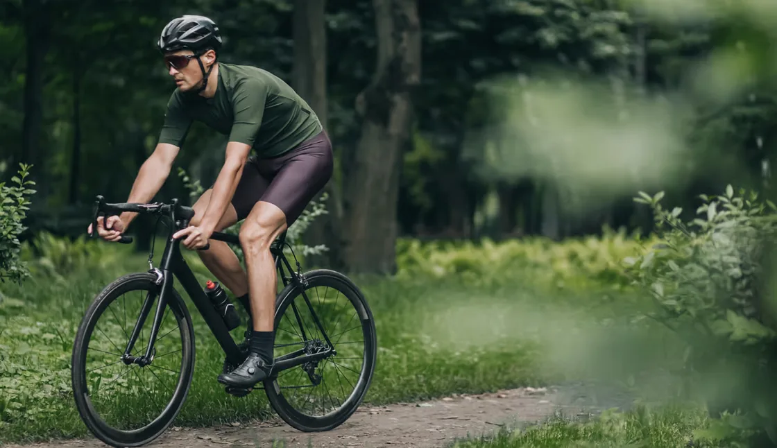 Radfahrer im olivgrünen Trikot auf einem Waldweg in voller Fahrt