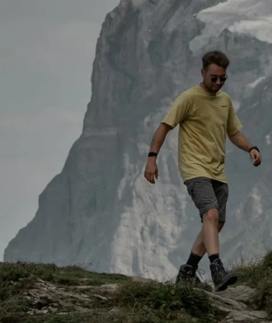 Wanderer im gelben Shirt steigt einen Grasgrat ab, vor ihm eine hohe Felswand